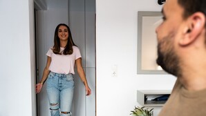 A person walking into a room with a TV and a fruit bowl on a table.