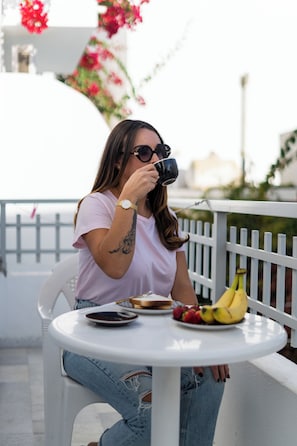 A person sitting at a white table with a plate of food, a banana, and a drink.