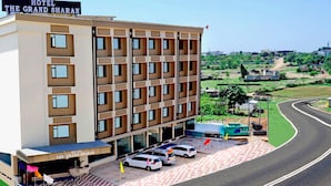 A multi-story hotel with a sign reading "Hotel The Grand Sharan." It features a parking area with several cars and a road curving around the property. - The Grand Sharan (Reasi)