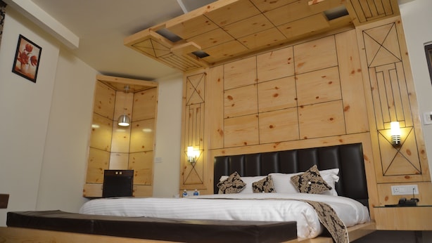 A hotel room with a wooden headboard, a bed with white linens, two wall-mounted lights, and a framed picture on the wall. - The Grand Sharan (Reasi)