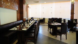 A restaurant with long communal tables, black leather booths, and a decorative wall. - The Grand Sharan (Reasi)