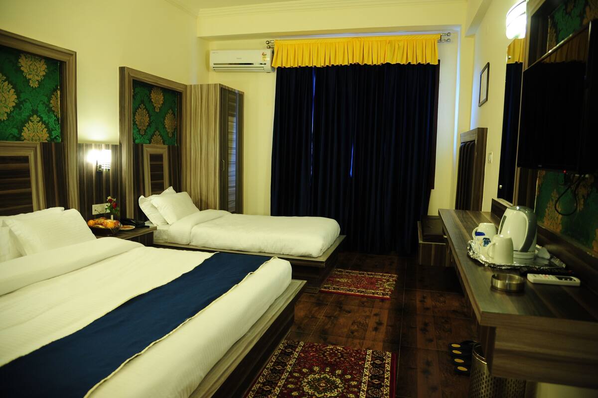 A hotel room with two beds, a desk with a kettle, a TV, and a window with curtains.