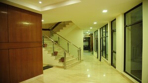 A modern interior with a wooden panel wall, a glass door, and a staircase with potted plants. - The Grand Sharan (Reasi)