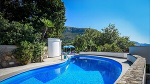 Piscina com borda de pedra, rodeada por vegetação e uma montanha ao fundo.