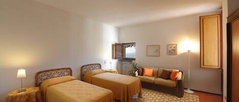 A hotel room with two beds, a sofa, a radiator, and a view of the sea.