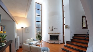 A spacious living room with a fireplace, a staircase, and a view of the outdoors.