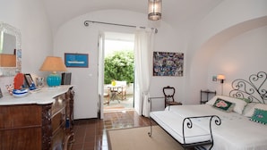 A bedroom with a bed, bedside table, lamp, and a view of the garden through an open door. - Casa Giardino (Positano)