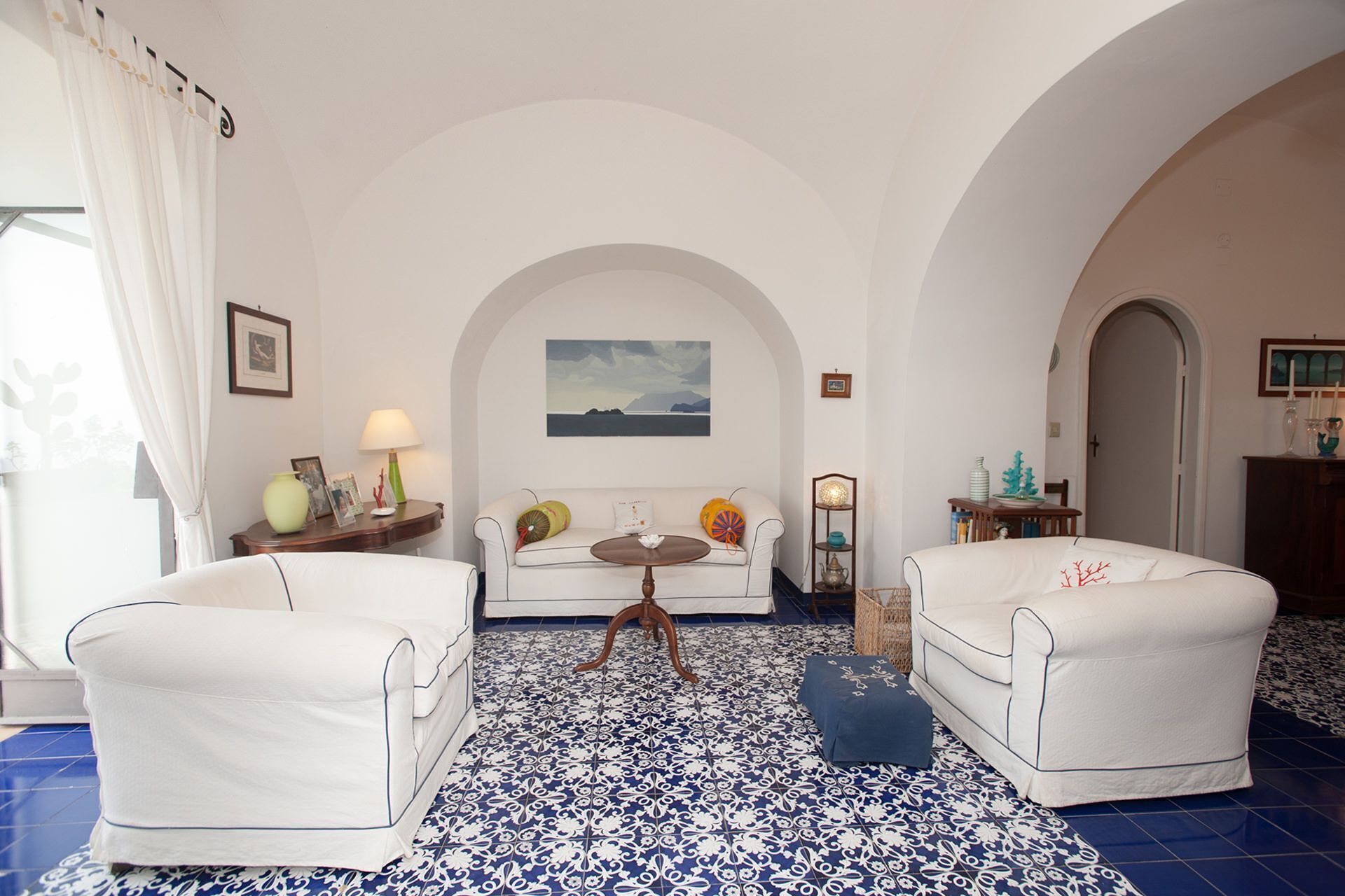 A room with a white sofa, two white armchairs, a small table, and a tiled floor.