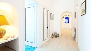 A hallway with white walls, a blue-tiled floor, and a door leading to a room with a blue-tinted window. - Casa Giardino (Positano)