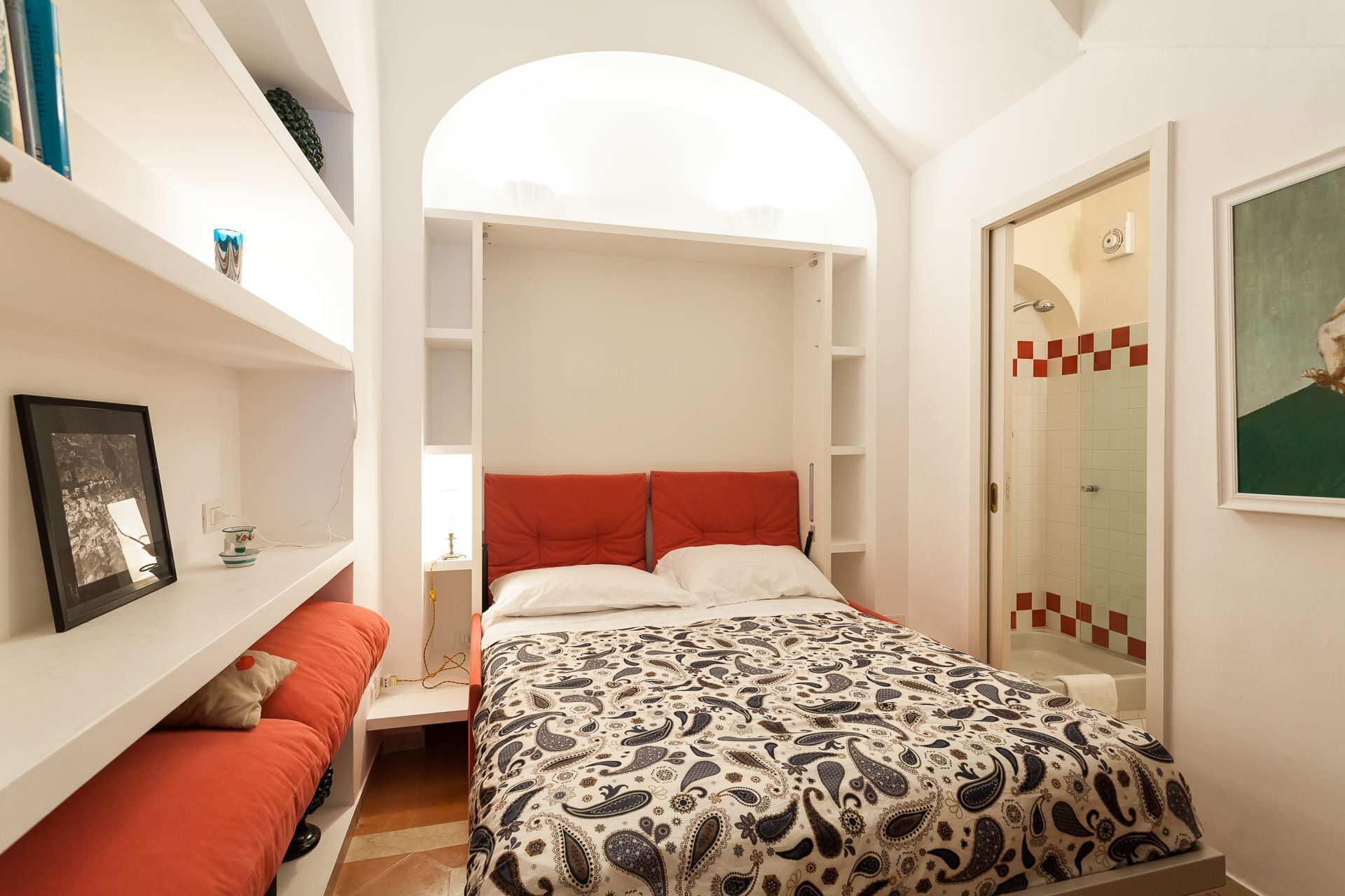 A bedroom with a bed, a built-in wardrobe, a shower area, and a small seating area with a sofa.