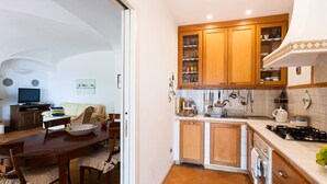 A compact kitchen with wooden cabinets, a dining area with a table and chairs, and a television in the living room. - Casa Dorothea 2 (Positano)