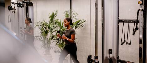 Un gimnasio con equipamiento de ejercicio, un espejo y plantas en macetas.