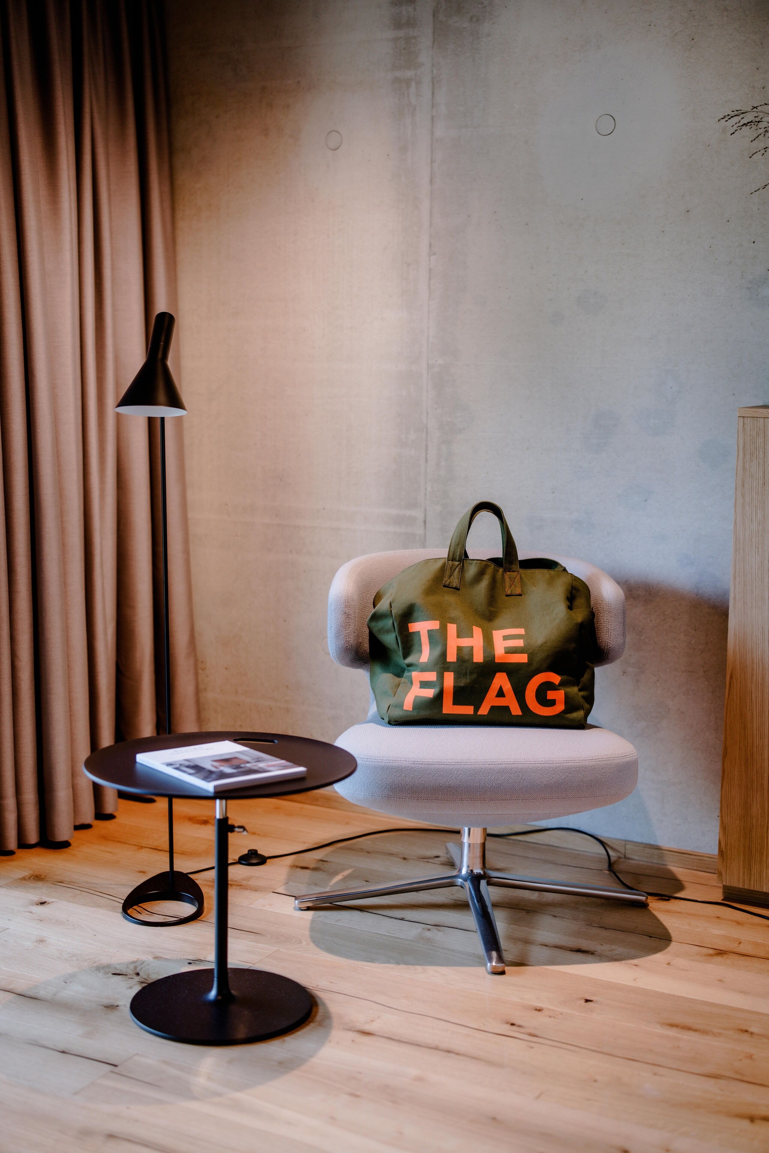 A modern room with a round table, a chair with a green bag labeled "THE FLAG", a floor lamp, and a wooden cabinet.