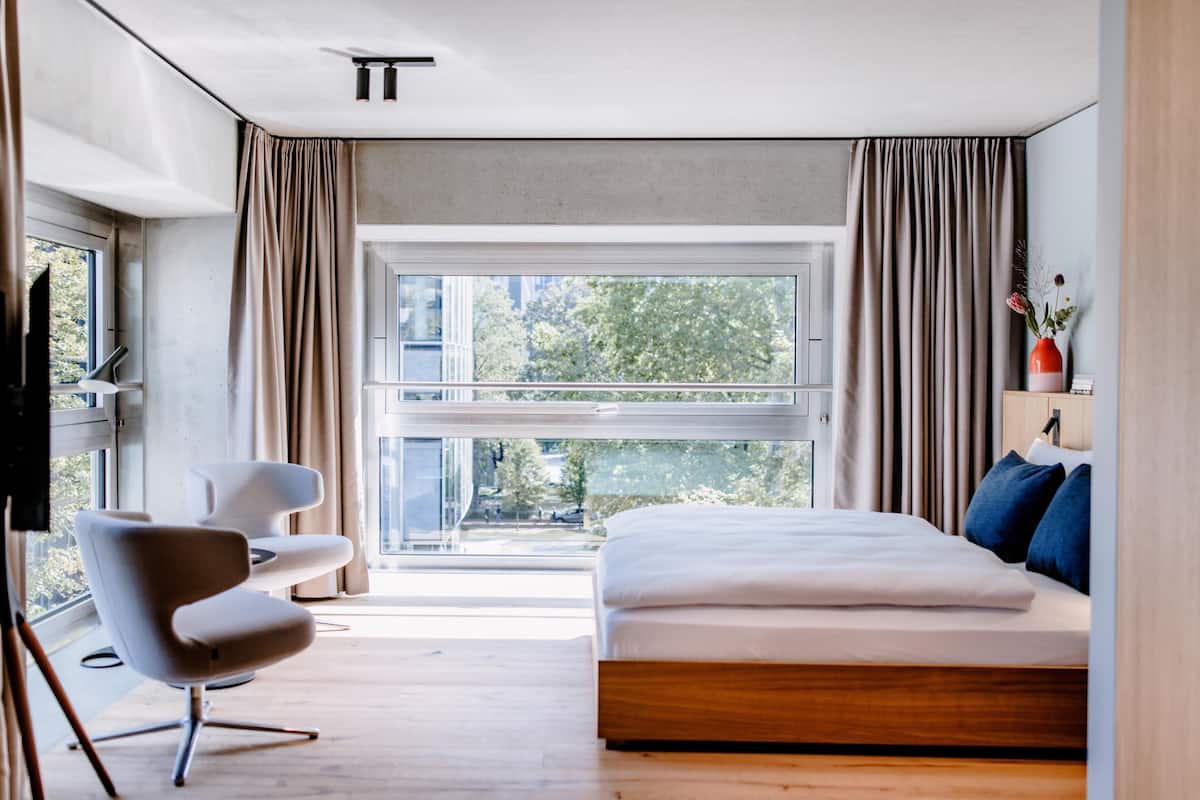 Ein modernes Schlafzimmer mit einem großen Bett, einem Sessel, einem Fernseher und einem Fenster mit Vorhängen.