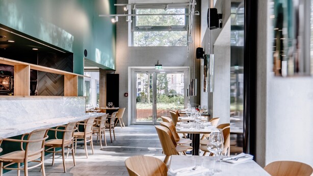 Un restaurant moderne avec un long comptoir, des chaises en bois et une vue sur l’extérieur.