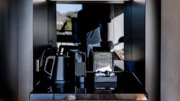 A compact kitchen with a wooden shelf holding cups and a wine glass, a coffee maker, and a small refrigerator.