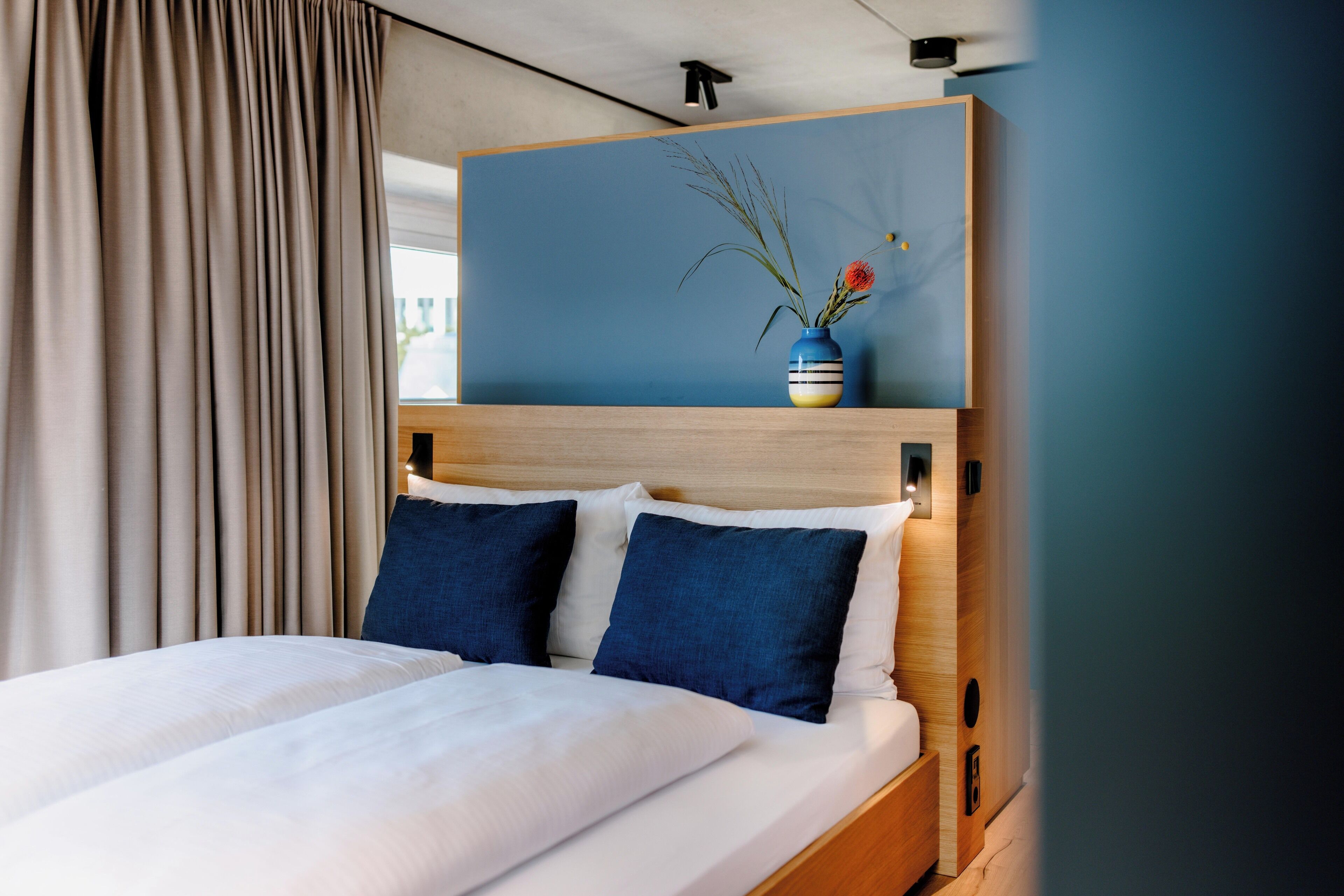 Een hotelkamer met een bed, een houten hoofdbord, een vaas met bloemen en uitzicht op het omliggende landschap.