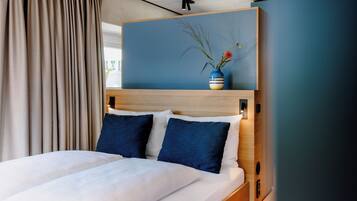 Een hotelkamer met een bed, een houten hoofdbord, een vaas met bloemen en uitzicht op het omliggende landschap.