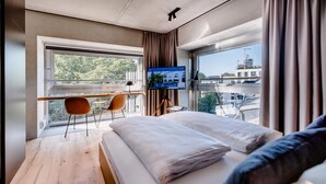 Une chambre d’hôtel moderne, équipée d’un lit, d’un bureau et d’une grande fenêtre donnant sur la ville.