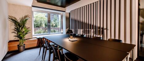 A conference room with a long table, chairs, a potted plant, and a window with blinds.