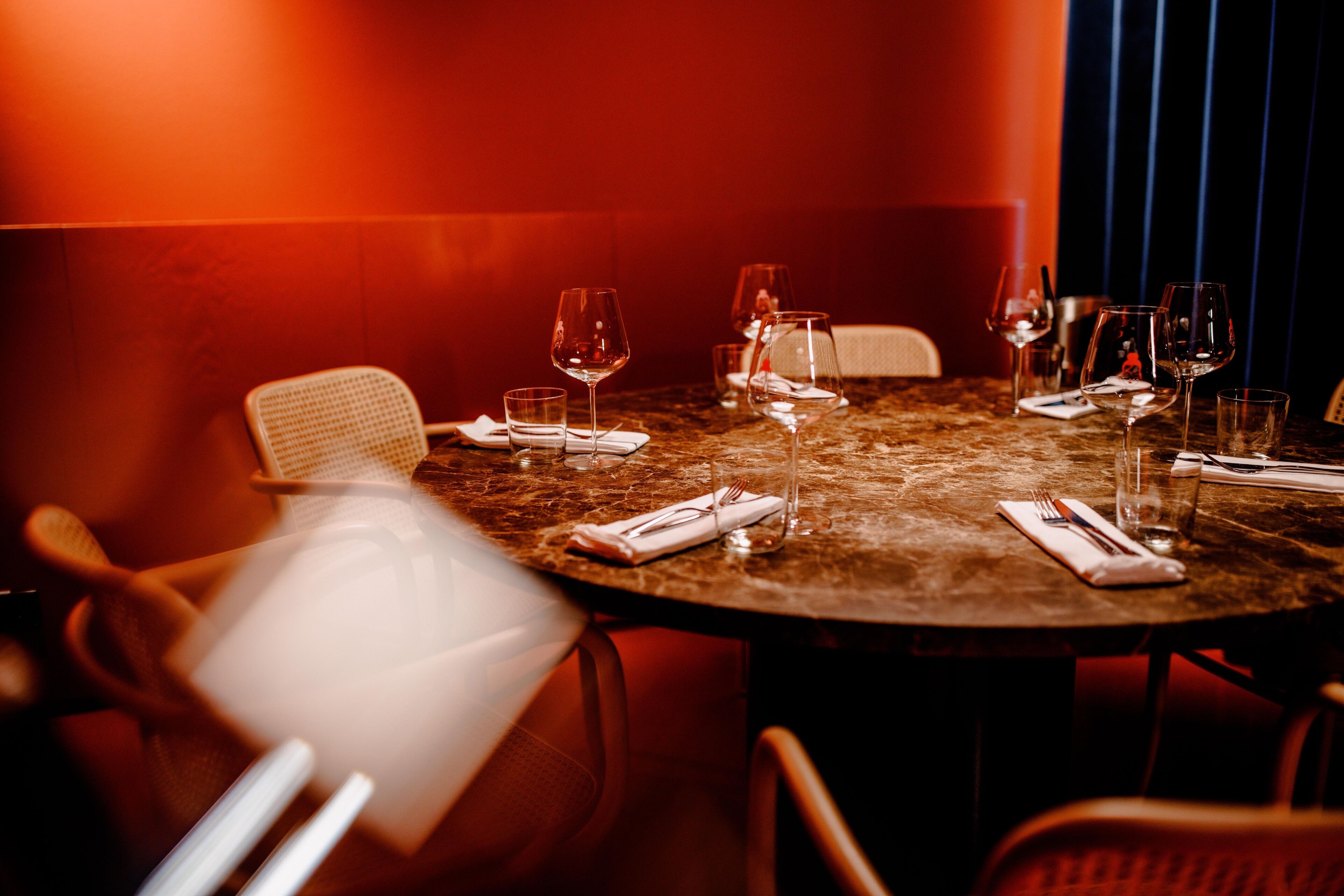 A round dining table with multiple wine glasses and cutlery, set against a red wall.