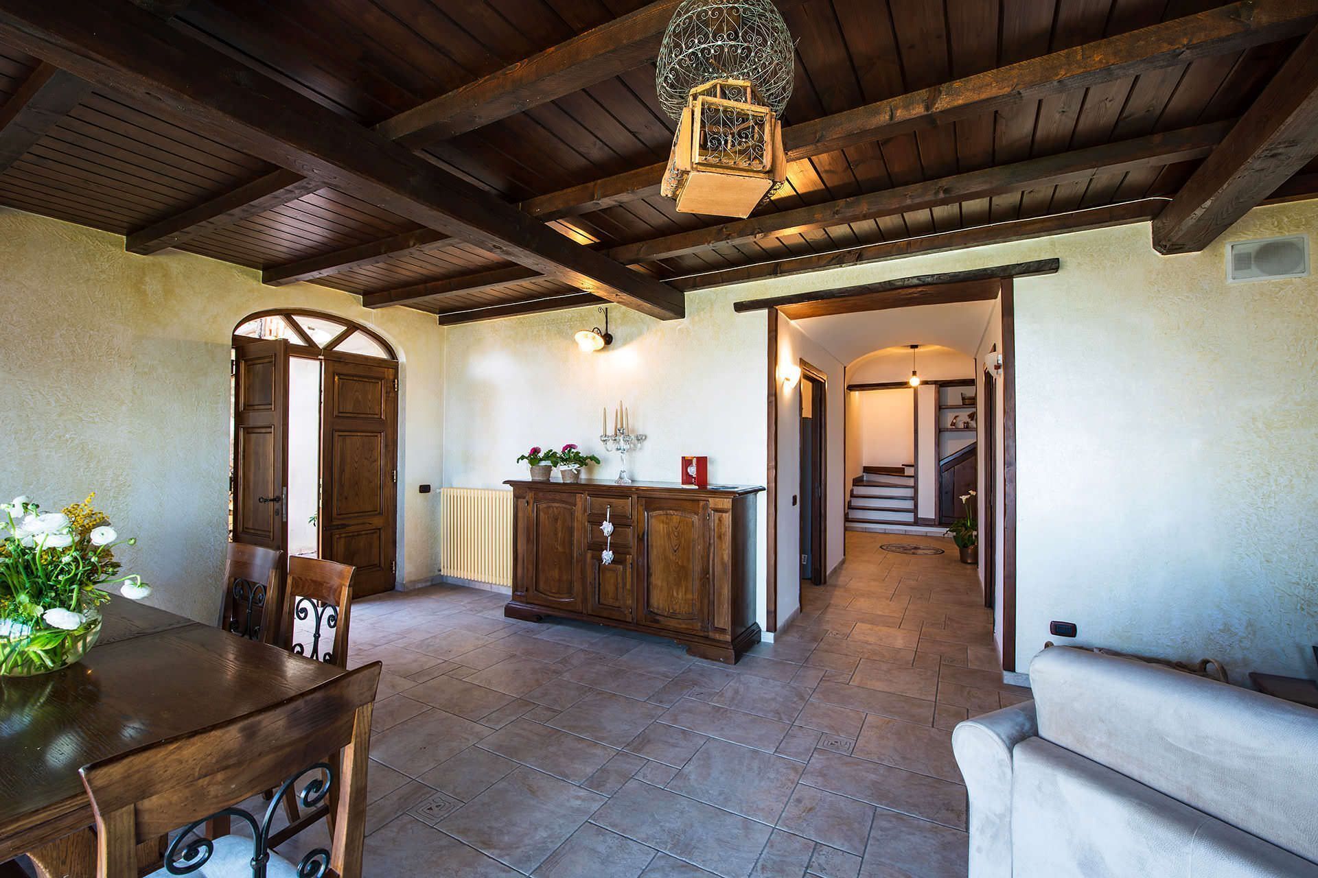 Quarto espaçoso com teto de madeira, mesa de jantar com cadeiras, sofá, armário com plantas em vasos e escada que dá acesso a outro espaço.