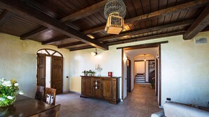 A spacious room with a wooden ceiling, a dining table with chairs, a sofa, a cabinet with potted plants, and a staircase leading to another area. - Villa Pandora (Sorrento)