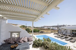A poolside area with a pergola, lounge chairs, and a view of the landscape. - Marvi House 1 (Mykonos)