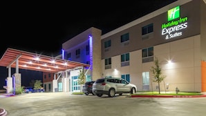 A Holiday Inn Express & Suites building with a covered parking area, multiple cars parked, and a well-lit facade. - Holiday Inn Express & Suites Leander by IHG (Leander)