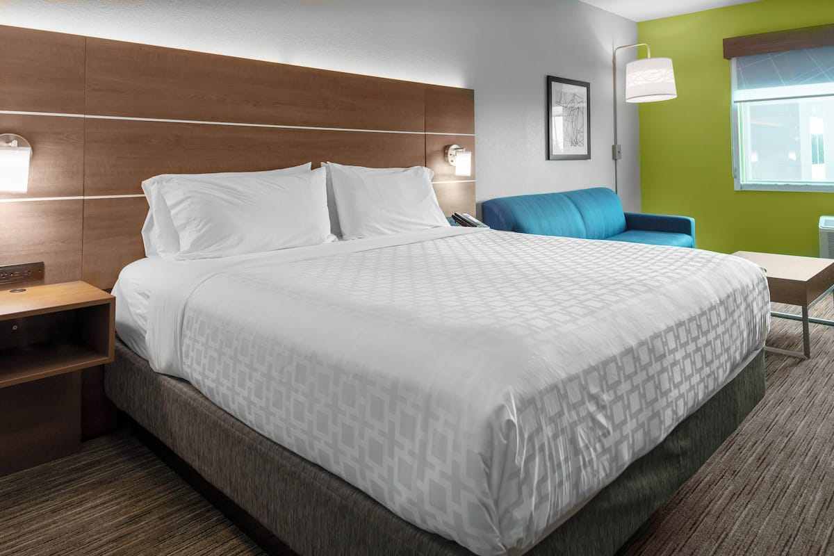 A hotel room with a large bed, a desk, a chair, and a window.