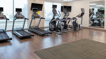 Une salle de sport équipée de tapis de course, de vélos elliptiques et d’un grand miroir.