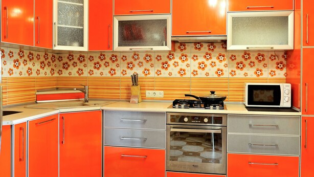 A kitchen with orange cabinets, a microwave, a stove, and a sink. - Description of Staroreznichnaya 28 (Odessa)