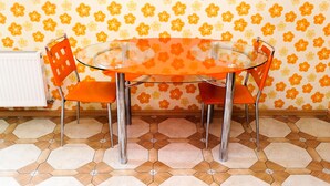 A dining area with a glass table and orange chairs, a radiator, and a patterned wall. - Description of Staroreznichnaya 28 (Odessa)