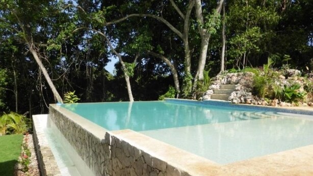 A swimming pool with a stone wall and a grassy area. - Exquisite Taste Awaits you With This Custom Styled Villa (Sosúa)