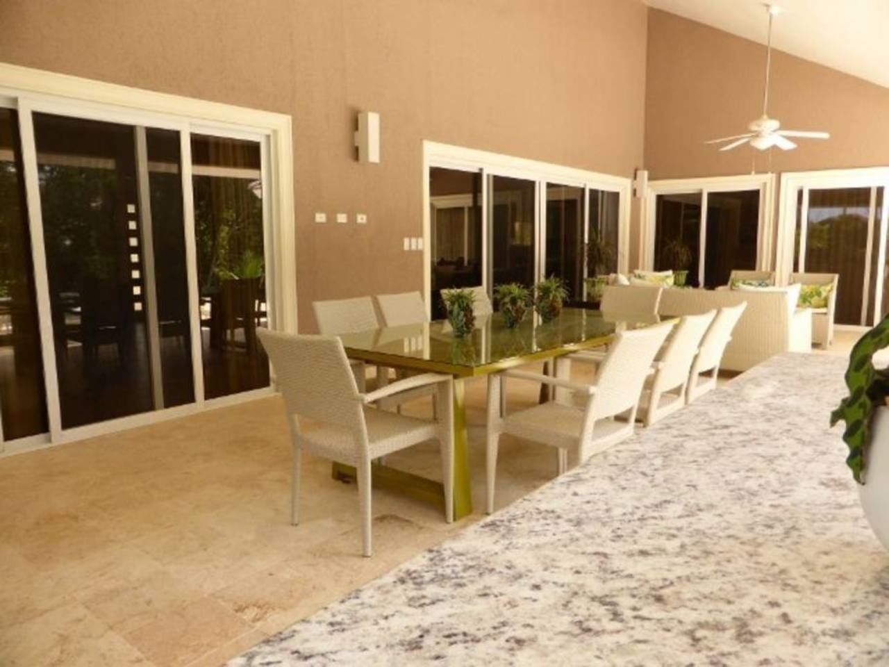A dining area with a glass table and chairs, large sliding glass doors, and a ceiling fan.