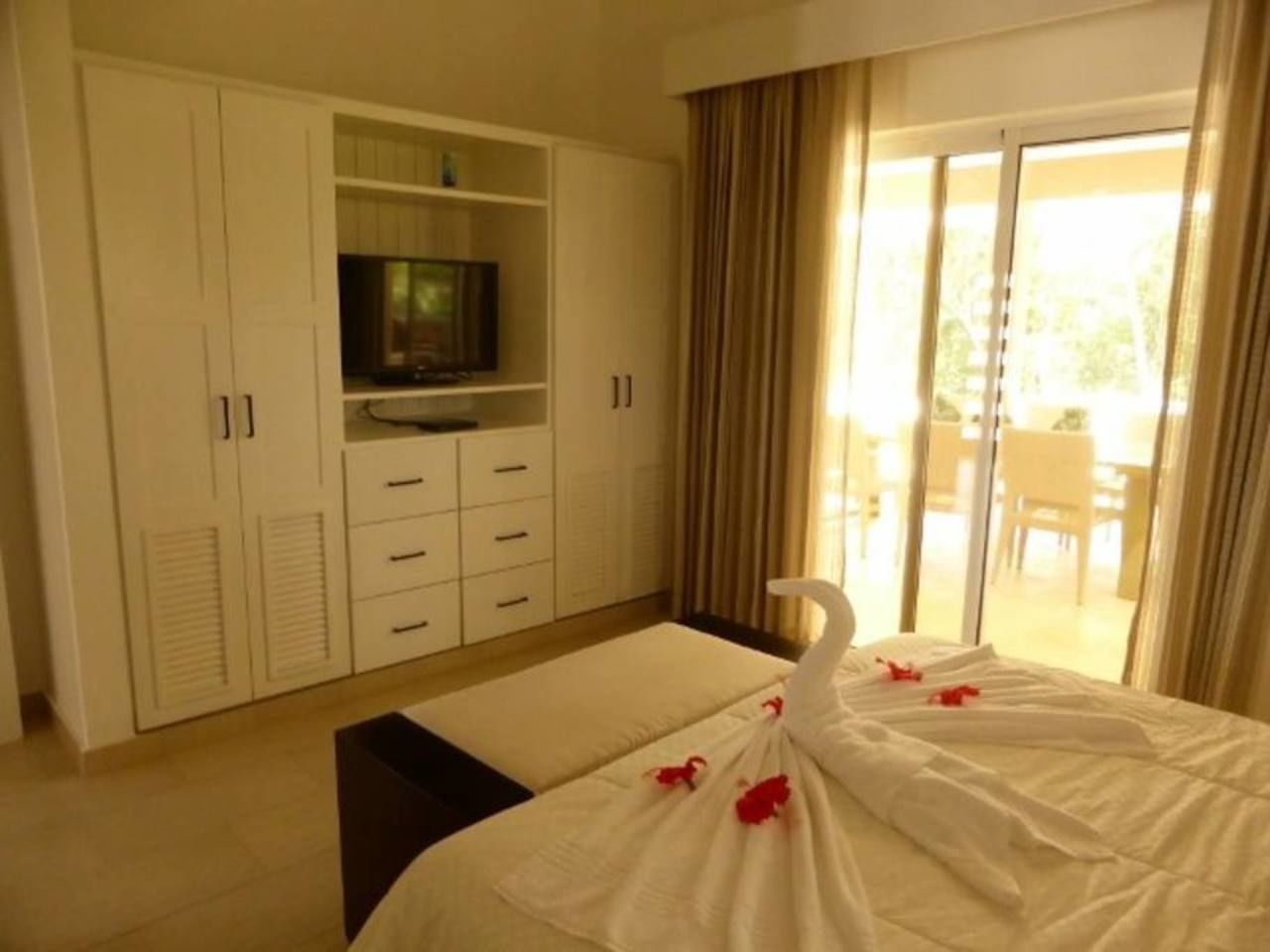 Une chambre d’hôtel avec un lit, un téléviseur posé sur un meuble et un balcon avec des rideaux.