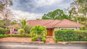 A two-story house with a red-tiled roof, surrounded by lush greenery and a paved driveway. - Exquisite Taste Awaits you With This Custom Styled Villa (Sosúa)