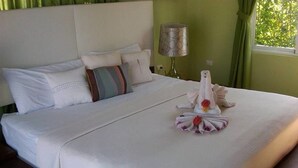 Una cama bien hecha con edredón blanco, una almohada con estampado a rayas y una toalla decorativa con flores.