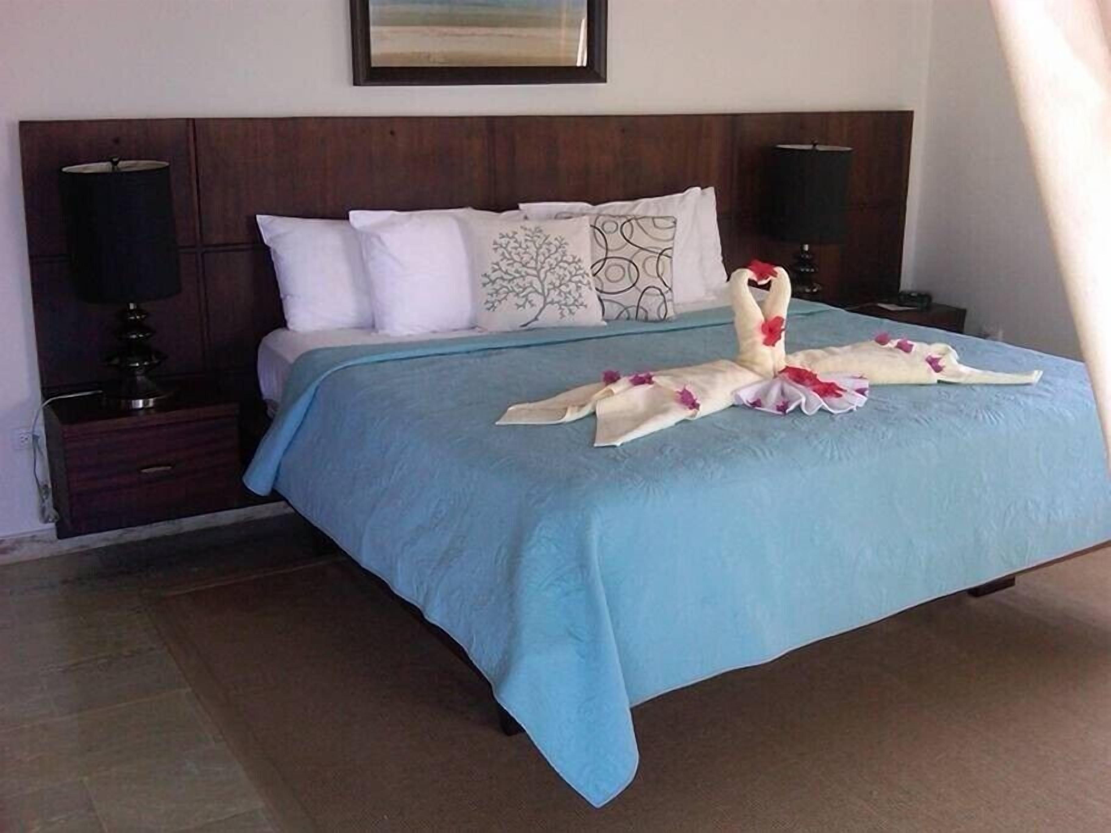 A neatly made bed with a blue bedspread and decorative towels arranged in a swan shape.