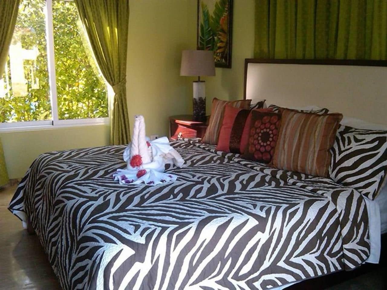 Un lit recouvert d’une couvre-lit à motifs zébrés, une table de chevet avec une lampe et une fenêtre avec des rideaux.