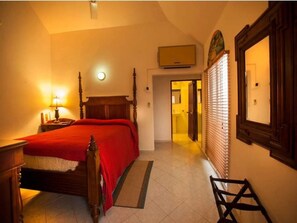 A bedroom with a wooden bed, a nightstand, a lamp, a wall-mounted TV, and a door leading to another room.