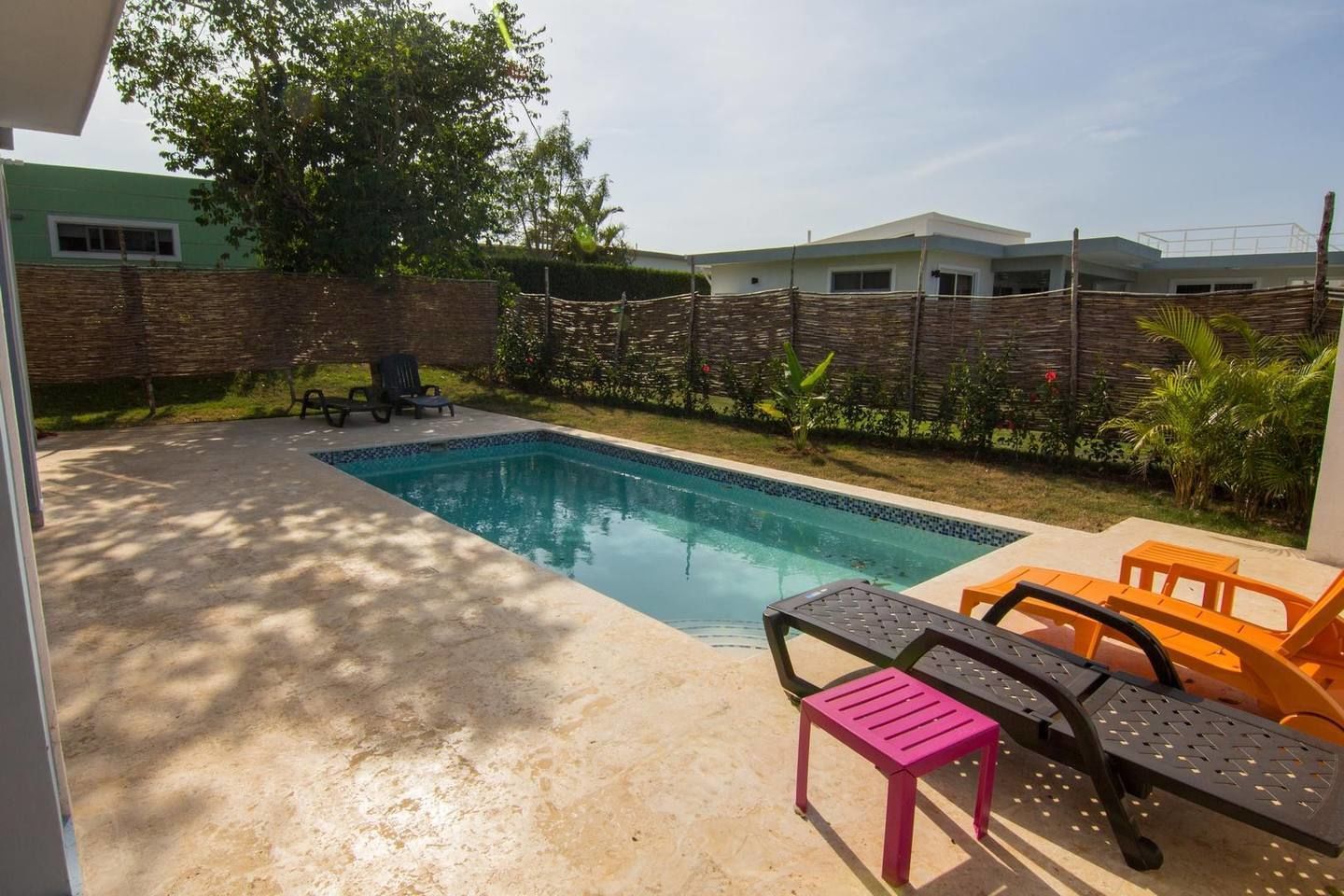 A swimming pool with a tiled edge, surrounded by a concrete deck. There are two lounge chairs and a small table.