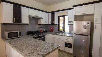 A kitchen with white cabinets, a granite countertop, a stainless steel refrigerator, a microwave, a stove, and a window with a view of the outside.