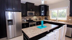 A modern kitchen with dark cabinets, stainless steel appliances, a granite countertop, and a window providing natural light. - Private and Spacious 5 Bedroom Villa (Sosúa)