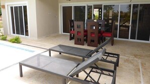 Een terras buiten met een zwembad, een tafel met stoelen en een plafondventilator.
