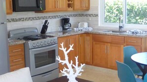 Une cuisine avec des meubles en bois, un four à micro-ondes, une cuisinière et une machine à café. On y trouve une table avec des chaises et un objet décoratif en forme de corail blanc.