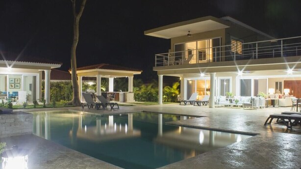 Une maison moderne à deux étages, dotée d’une piscine, d’un espace extérieur aménagé et d’un patio bien éclairé.