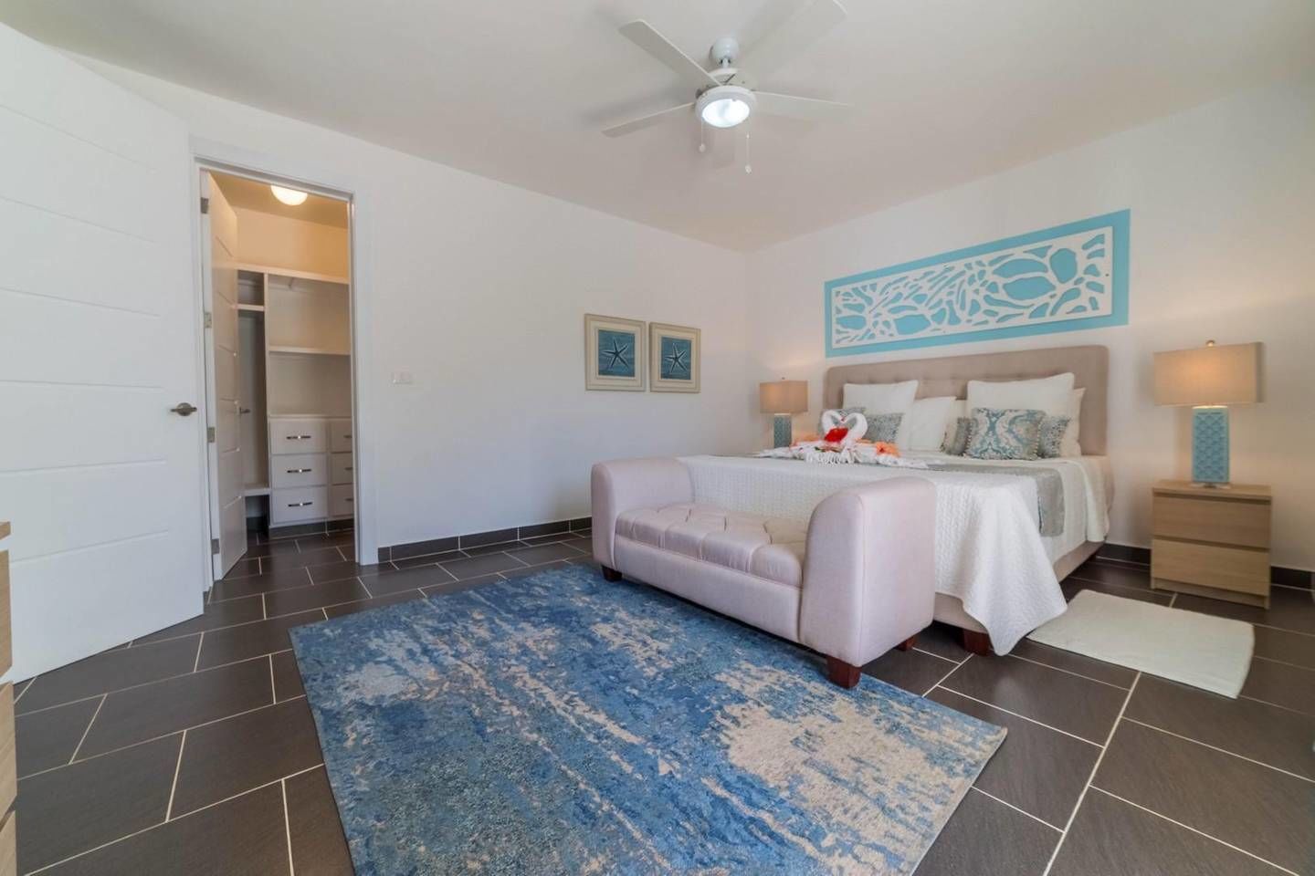 A bedroom with a bed, a nightstand, a ceiling fan, a door leading to a closet, and a blue rug.