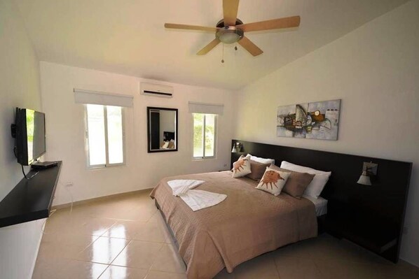 Un dormitorio con cama, ventilador de techo, televisor y ventana.