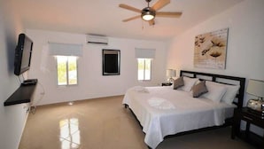 A bedroom with a bed, a ceiling fan, a TV, and a window.